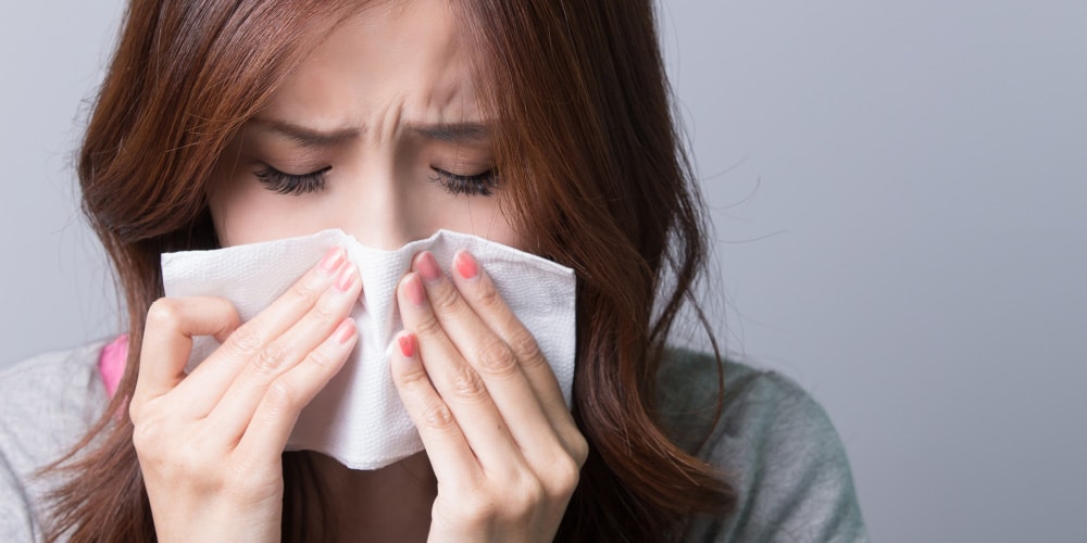 鼻をかみながら辛そうにする女性