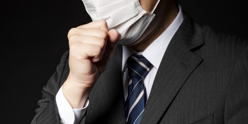 マスクをつけて辛そうに、せきをするスーツ姿の男性